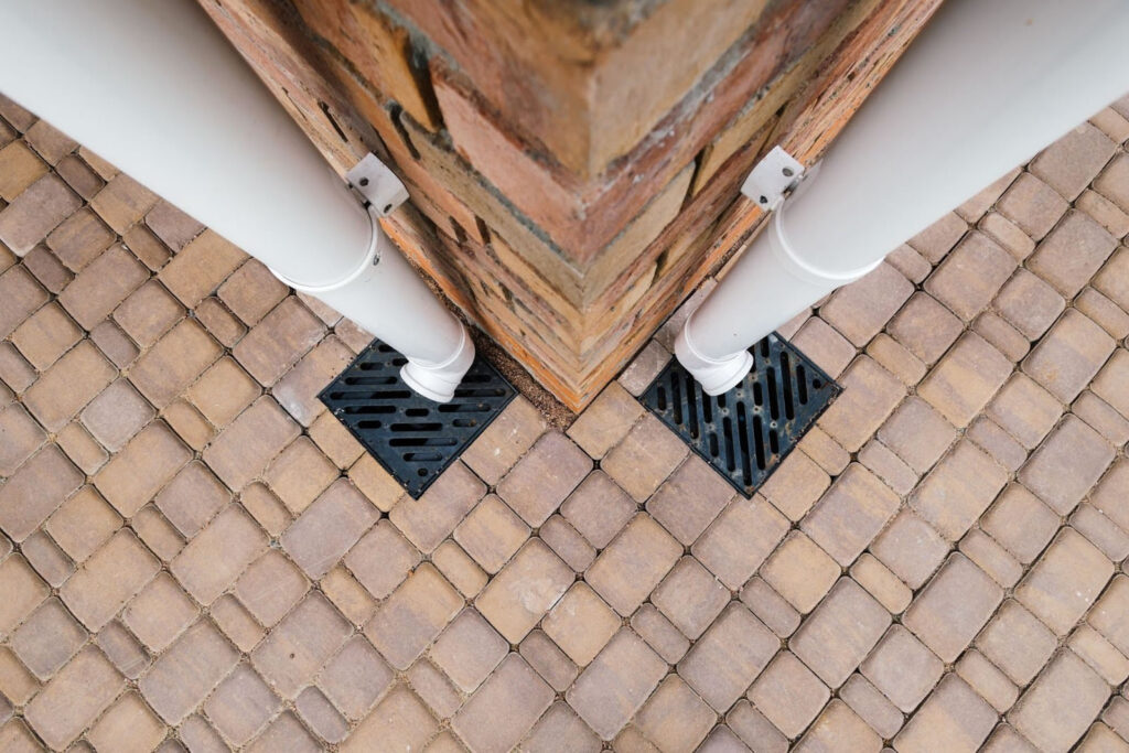 Close-up of downspouts connected to surface drains on paved patio to manage stormwater runoff